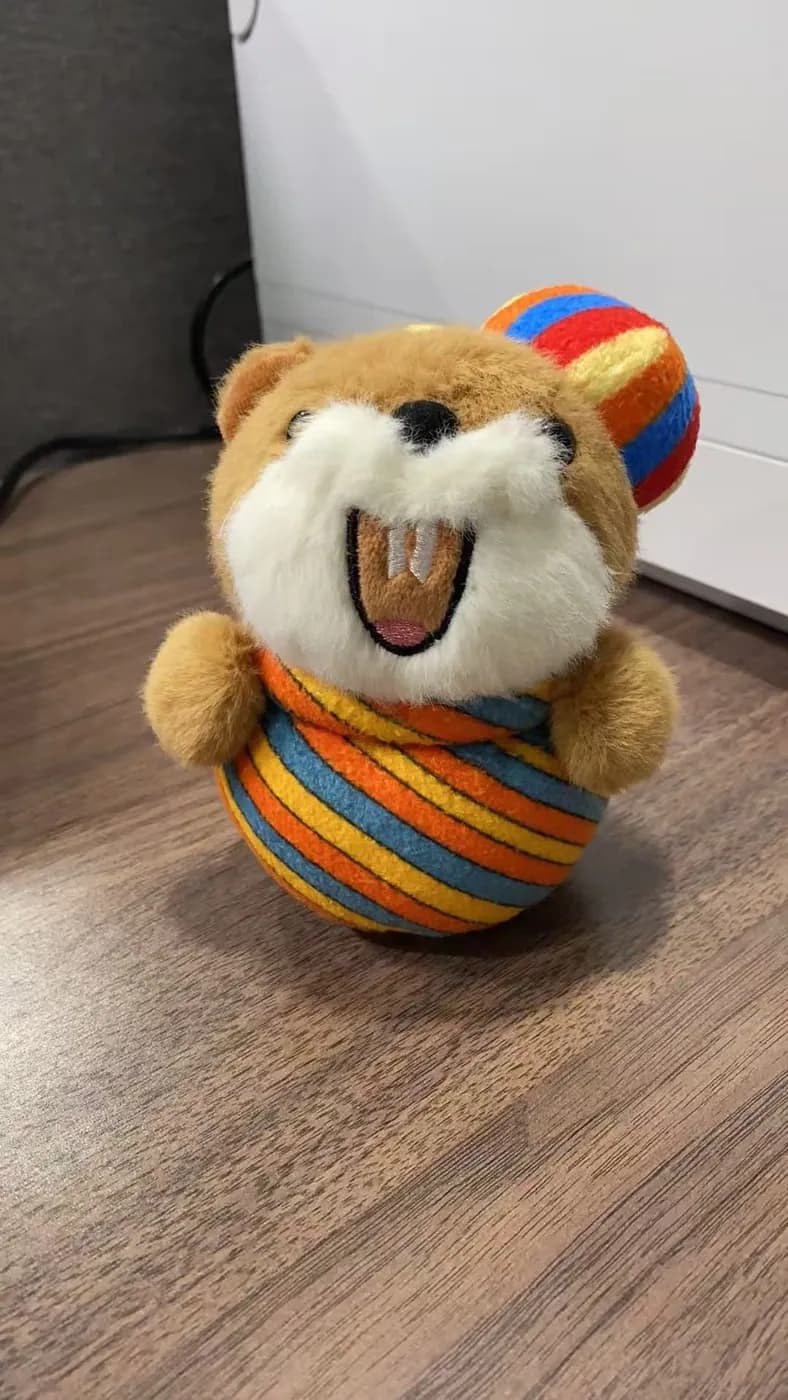 Bear plush toy holding a striped fabric ball