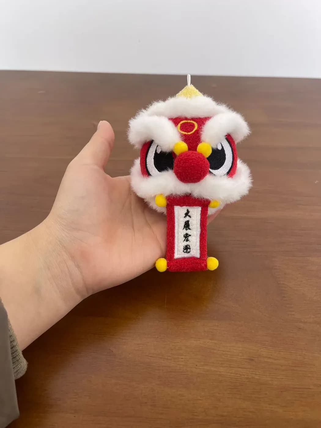 Lion dance plush keychain holding a printed red banner