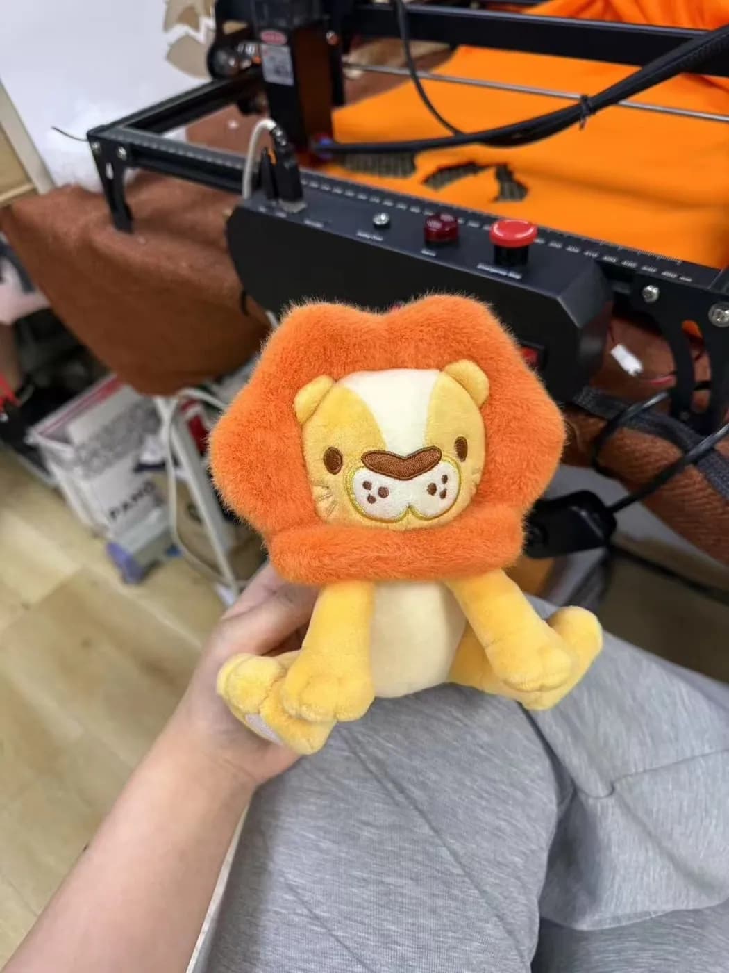 Orange lion plush charm with a dense mane and embroidered face