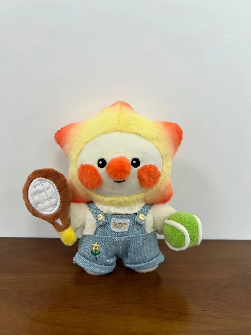 Bird mascot plush in dungarees holding a tennis racket
